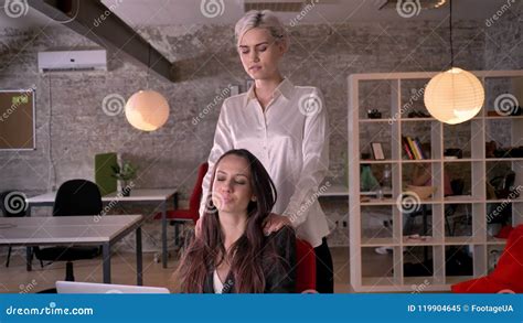 Young blonde lesbian massaging woman in modern office during .